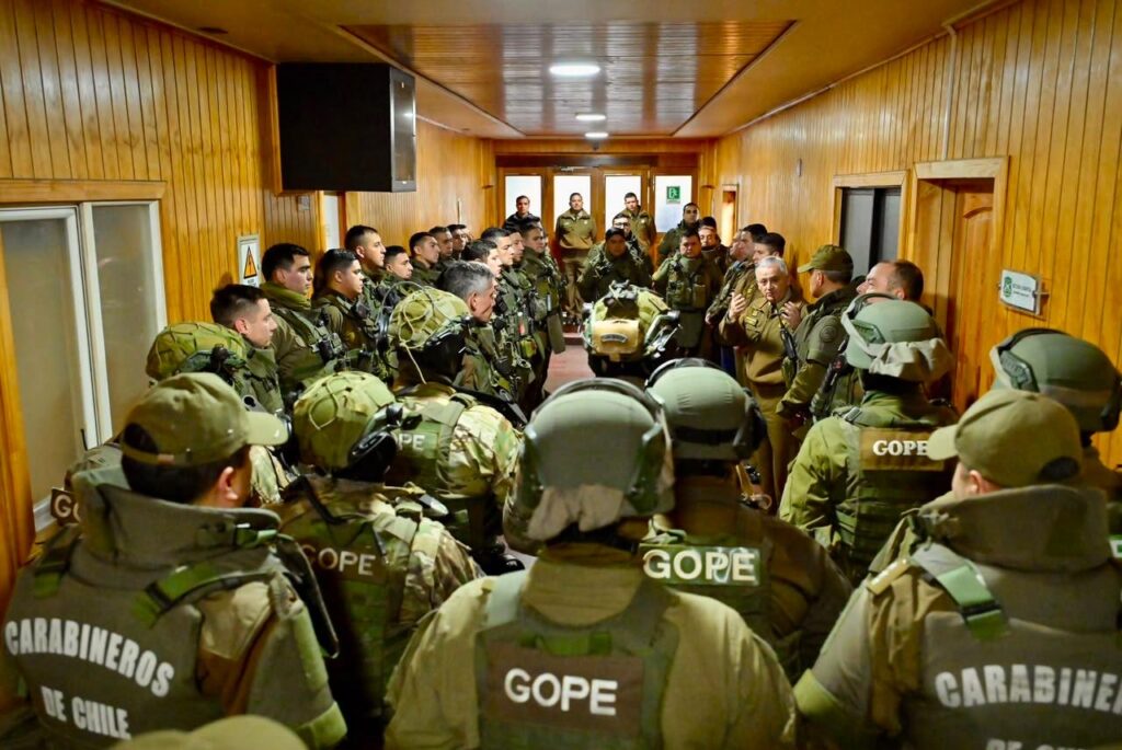 Funcionarios del GOPE de Carabineros, equipados con cascos y chalecos tácticos, escuchan a un alto oficial en el pasillo de un cuartel en Valdivia.