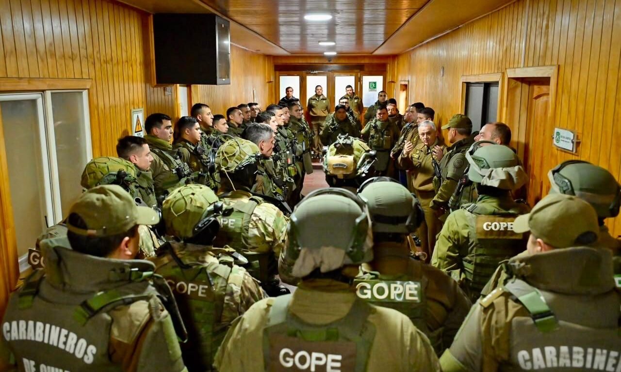 Funcionarios del GOPE de Carabineros, equipados con cascos y chalecos tácticos, escuchan a un alto oficial en el pasillo de un cuartel en Valdivia.