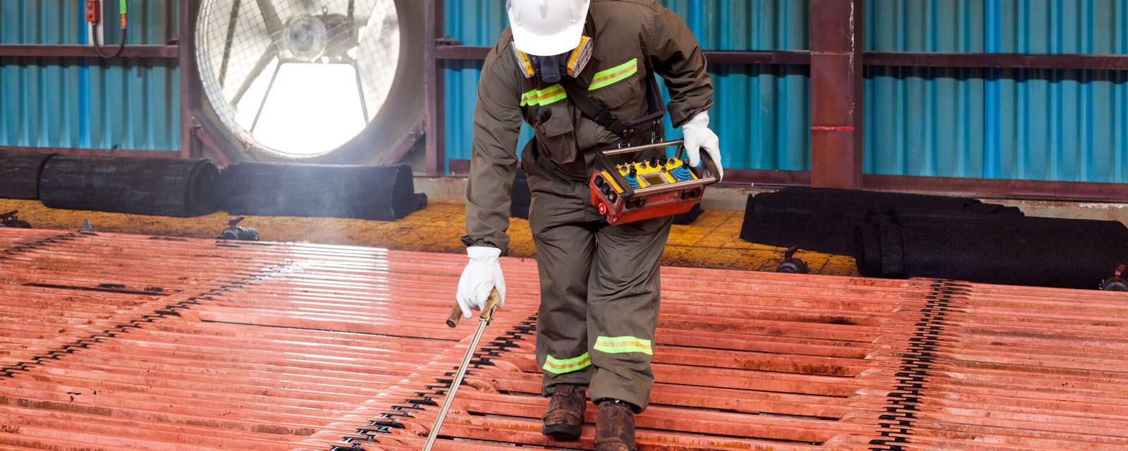 Trabajador con casco y traje de seguridad inspecciona cátodos de cobre en planta de procesamiento minero.