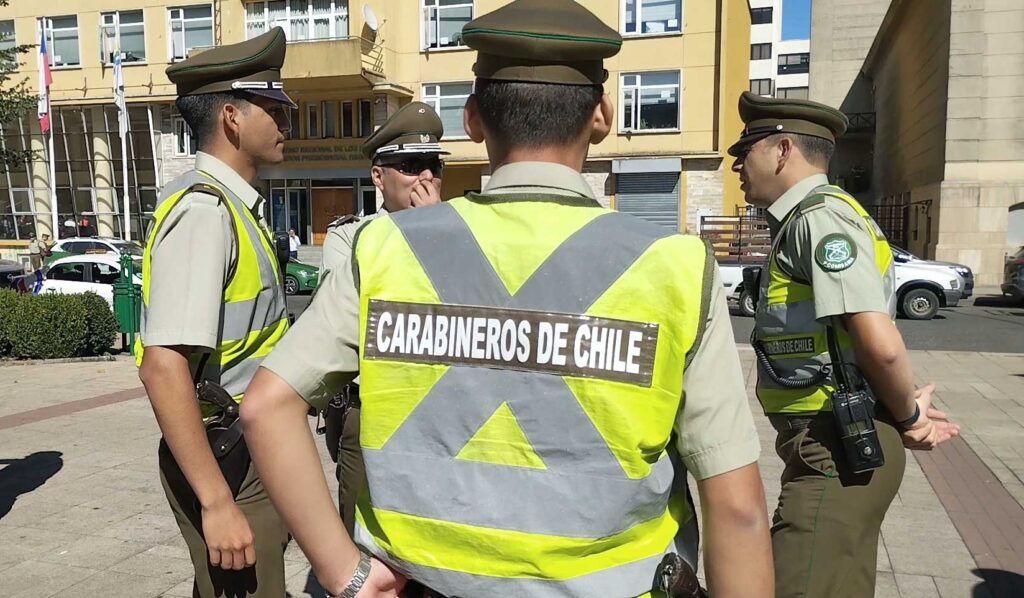 Cuatro carabineros con chalecos reflectantes conversan en una plaza de Valdivia, frente al edificio del Gobierno Regional de Los Ríos.