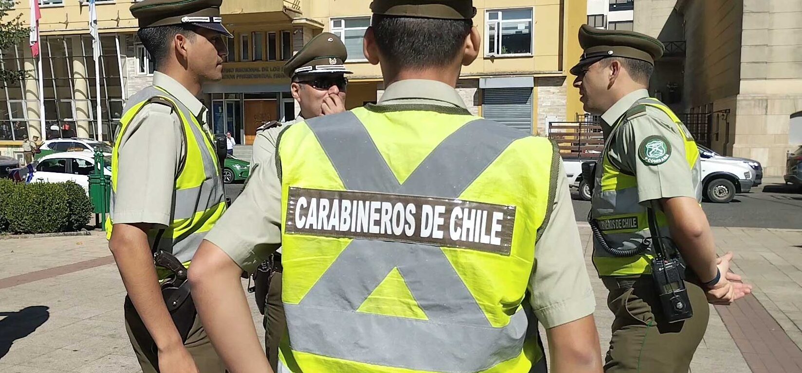Cuatro carabineros con chalecos reflectantes conversan en una plaza de Valdivia, frente al edificio del Gobierno Regional de Los Ríos.