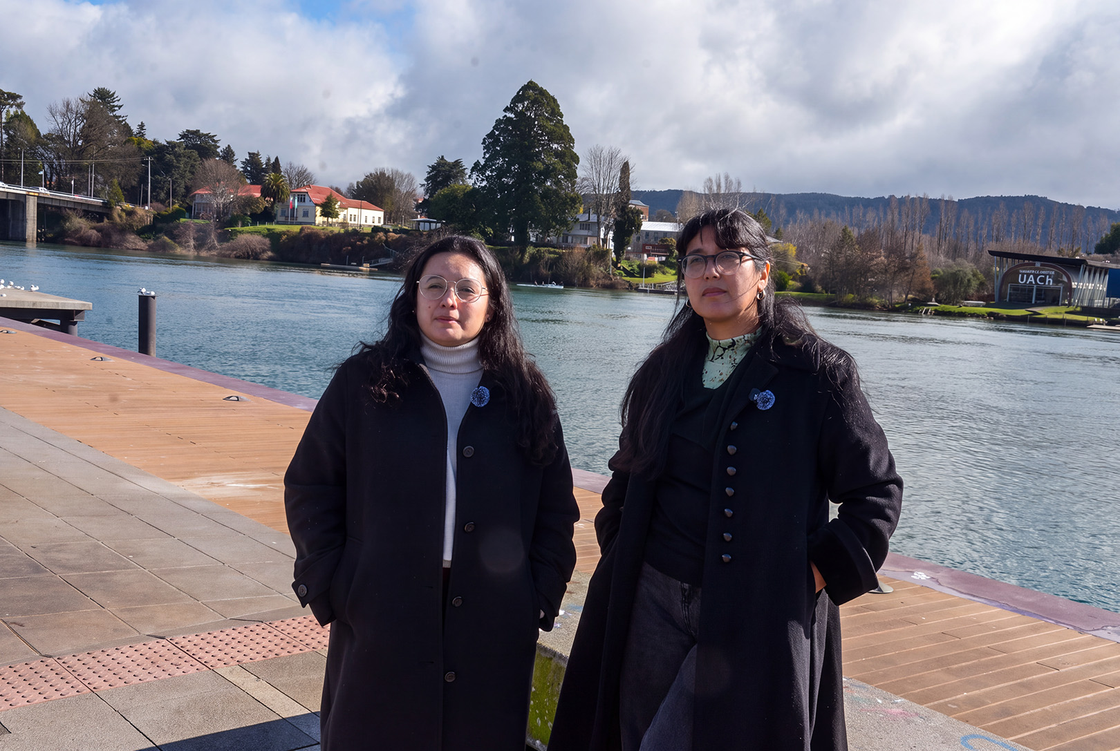 aola Jara Fernández y Lilian Guerra Arriagada, integrantes de Mujeres por Los Ríos, de pie en la Costanera de Valdivia frente al río Calle-Calle y la Isla Teja.