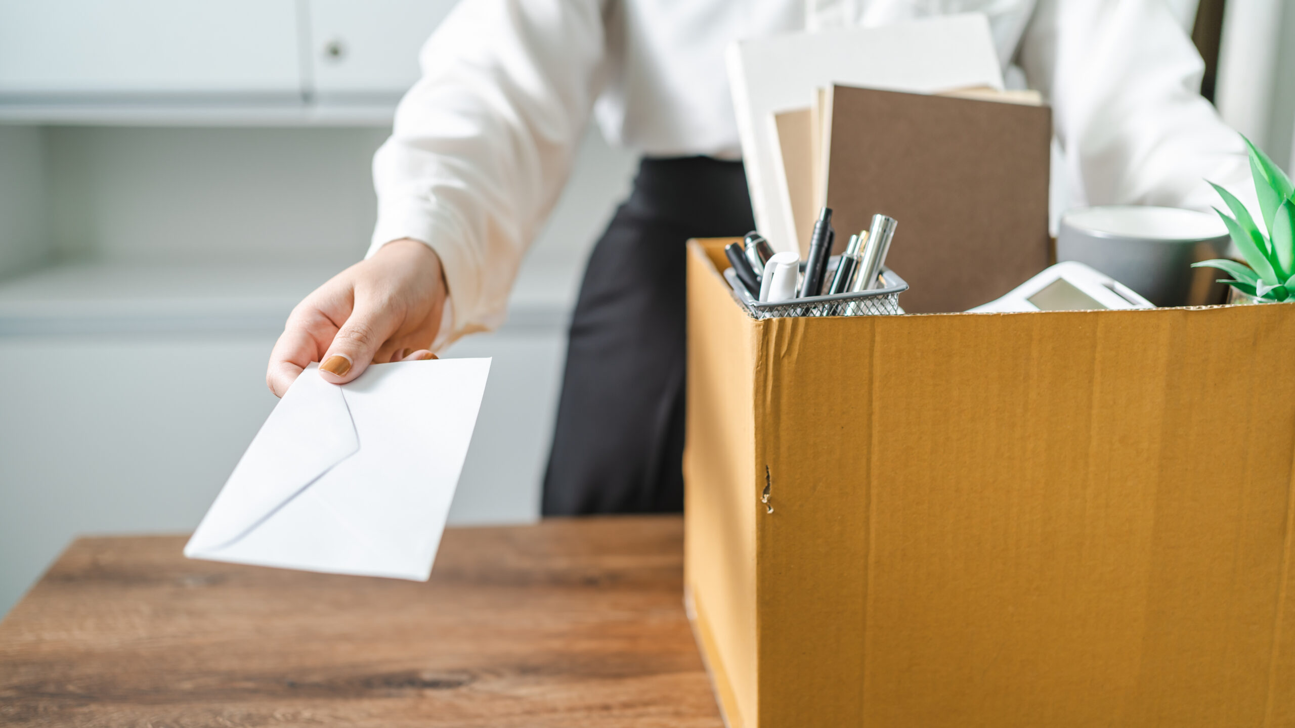 Persona sosteniendo una caja con pertenencias de oficina mientras entrega un sobre blanco