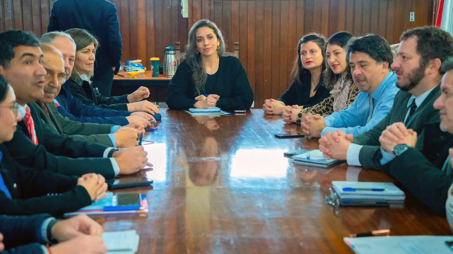 Grupo de personas sentadas alrededor de una gran mesa de madera durante una reunión de trabajo