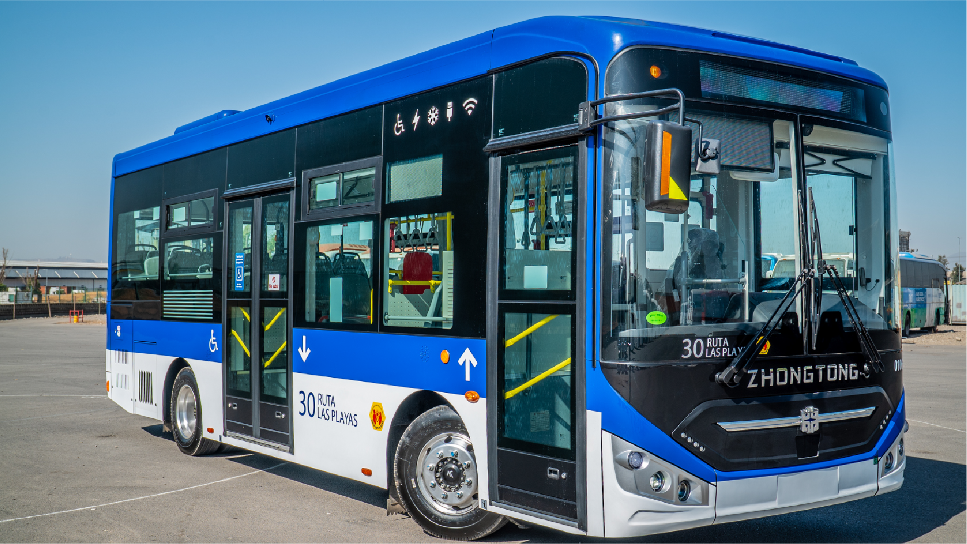 Fotografía de un moderno autobús urbano de color azul y blanco, marca Zhongtong, que representa el tipo de vehículo eléctrico para el transporte público que será financiado en Valdivia por el Gobierno Regional de Los Ríos. El vehículo, estacionado en una zona despejada, muestra letreros de ruta y varios íconos que indican características como accesibilidad para personas con discapacidad, puertos USB para carga, aire acondicionado y conexión Wi-Fi.