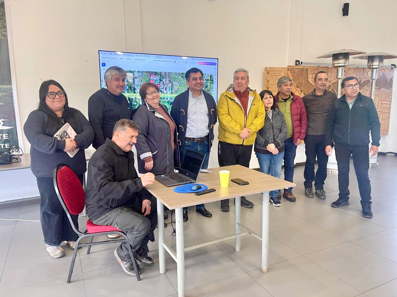Grupo de personas reunidas alrededor de un computador portátil durante una presentación con un mapa en pantalla