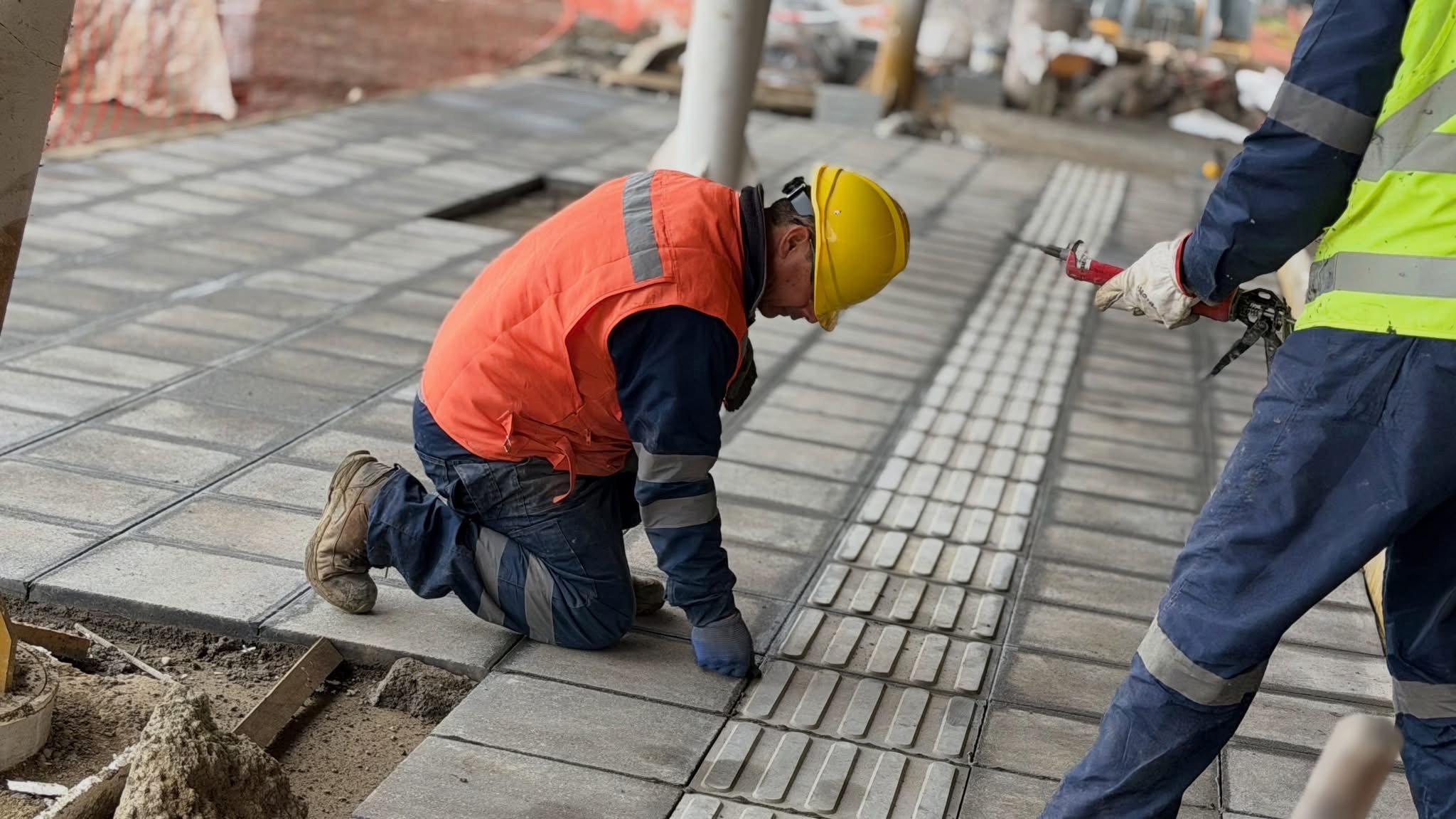 Trabajador de la construcción arrodillado instalando baldosas podotáctiles en una acera