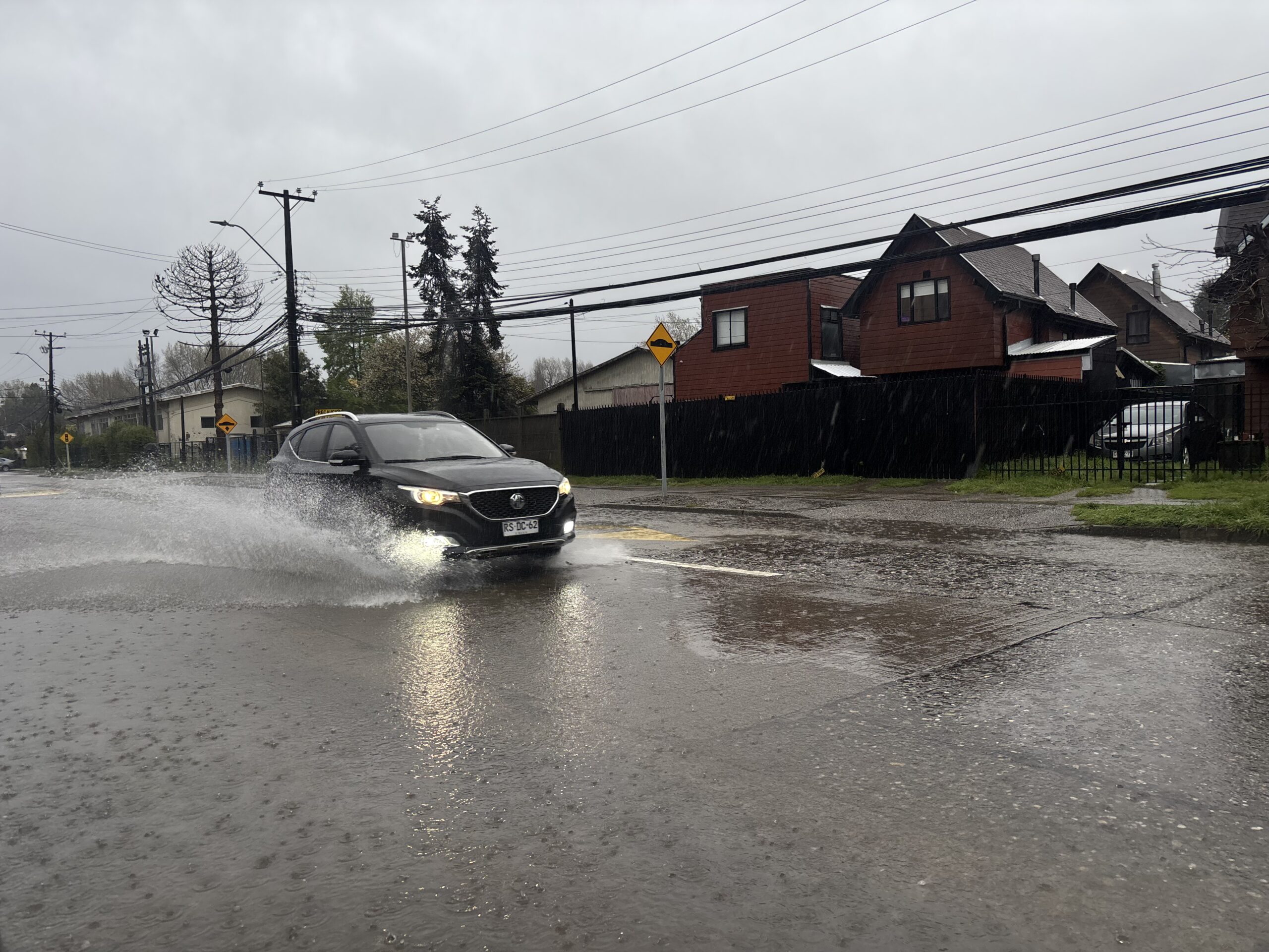 Auto negro circulando por una calle inundada en un día lluvioso, salpicando agua