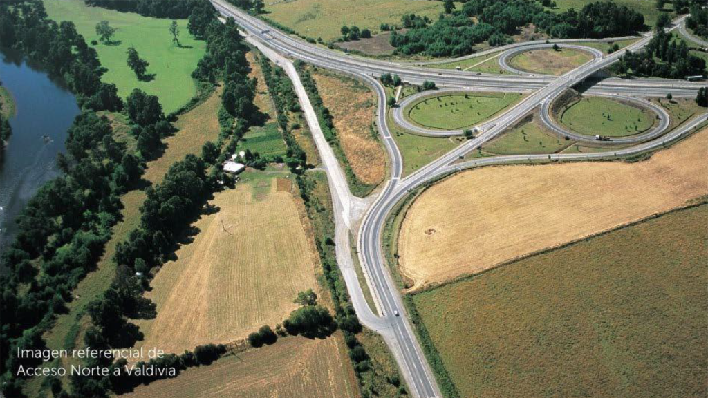 Vista aérea de un gran enlace de autopista en forma de trébol rodeado de campos agrícolas, un río y bosques. El texto superpuesto en la esquina inferior izquierda dice: “Imagen referencial de Acceso Norte a Valdivia”.