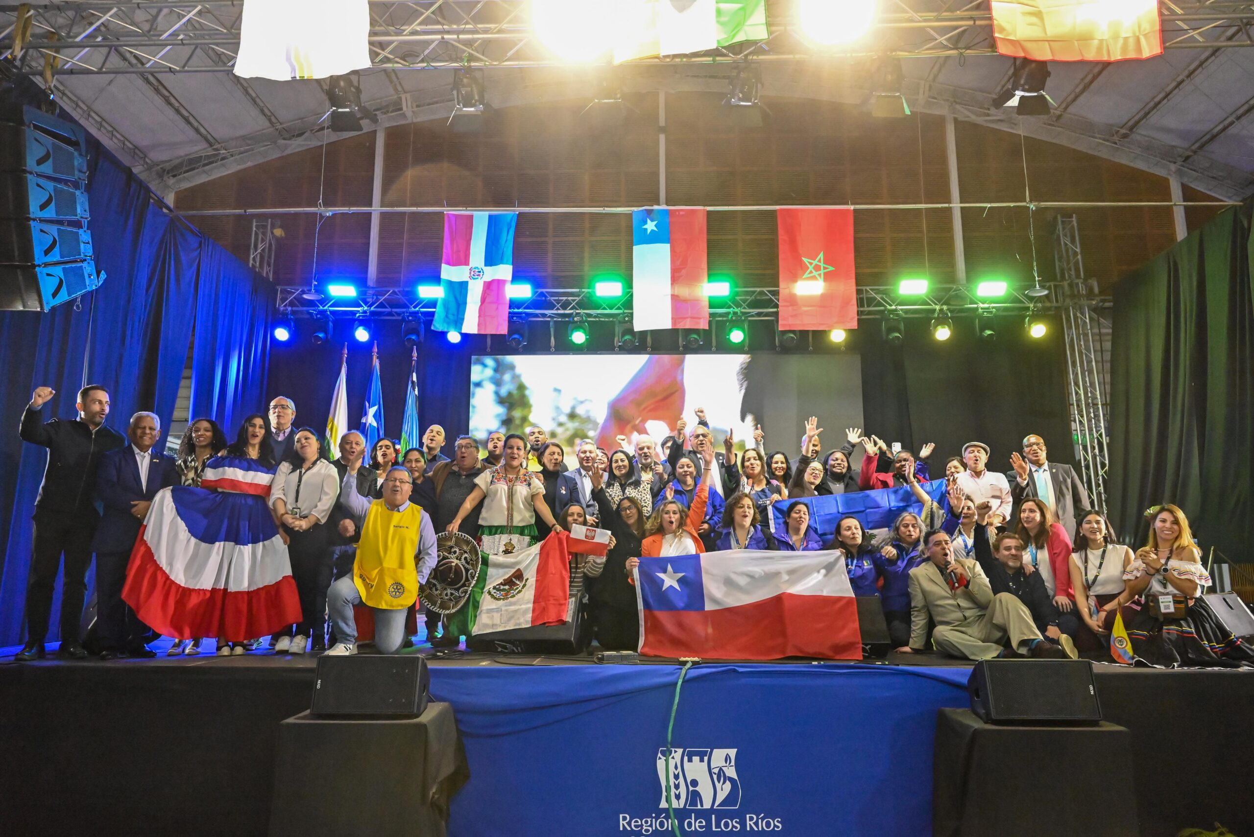 Grupo de personas en un escenario sosteniendo banderas de Chile, México y otros países en un evento de la Región de Los Ríos