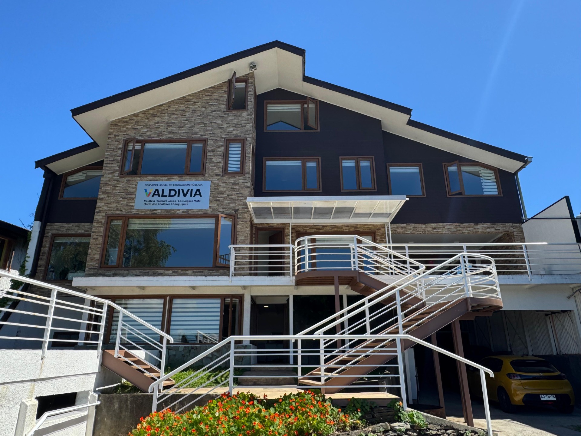 Edificio del Servicio Local de Educación Pública Valdivia con fachada de piedra, madera y escaleras exteriores blancas